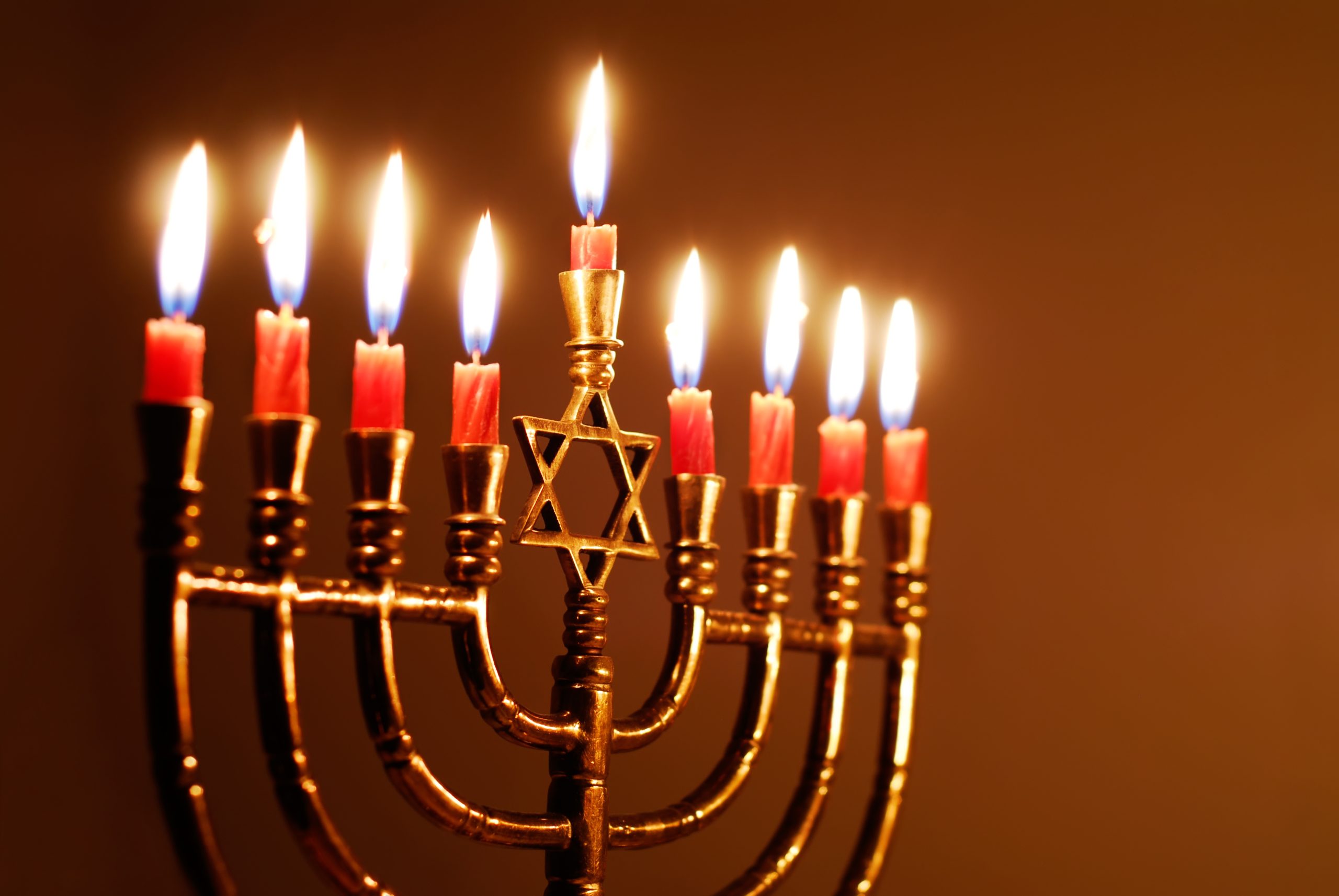 A brass menorah with nine lit candles, including the central shamash, glowing during a Hanukkah celebration.